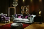 Κλασικό σαλόνι VIVALDI SOFA με ανοιχτόχρωμη επένδυση, καμπύλα μπράτσα και μωβ διακοσμητικά μαξιλάρια.