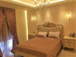 Κλασική κρεβατοκάμαρα HERMES με ανοιχτόχρωμο κρεβάτι, καπιτονέ κεφαλάρι και διακοσμητικό τελείωμα στην κορυφή.