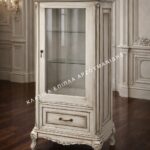 Κλασική βιτρίνα Verona Vitro σε ανοιχτή απόχρωση, με μία γυάλινη πόρτα, κάτω συρτάρι και καμπύλη βάση