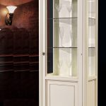 Κλασική βιτρίνα ENOS 1F σε ανοιχτή απόχρωση, με μία γυάλινη πόρτα, κλειστό κάτω τμήμα και λεπτά καμπύλα πόδια